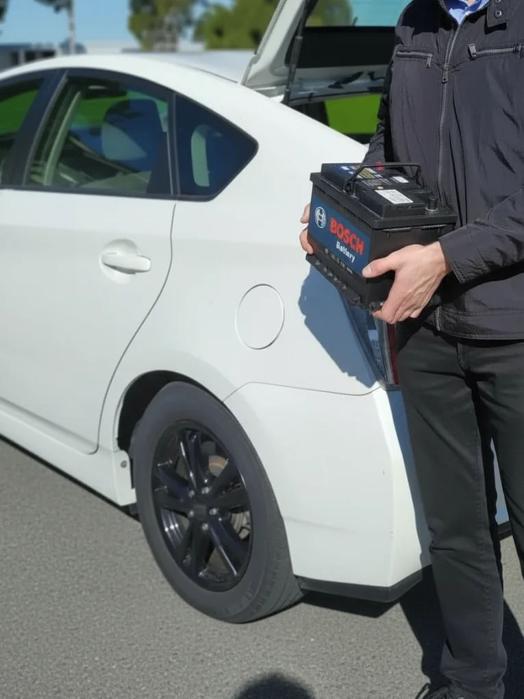 Man holding a Bosch battery beside a white hatchback with its bonnet open