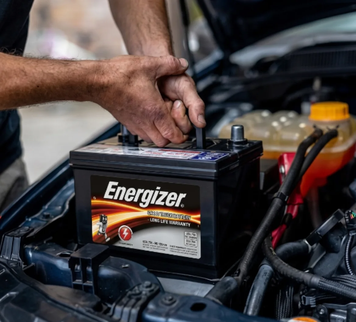 Hands on the terminals of a car battery in an open engine bay