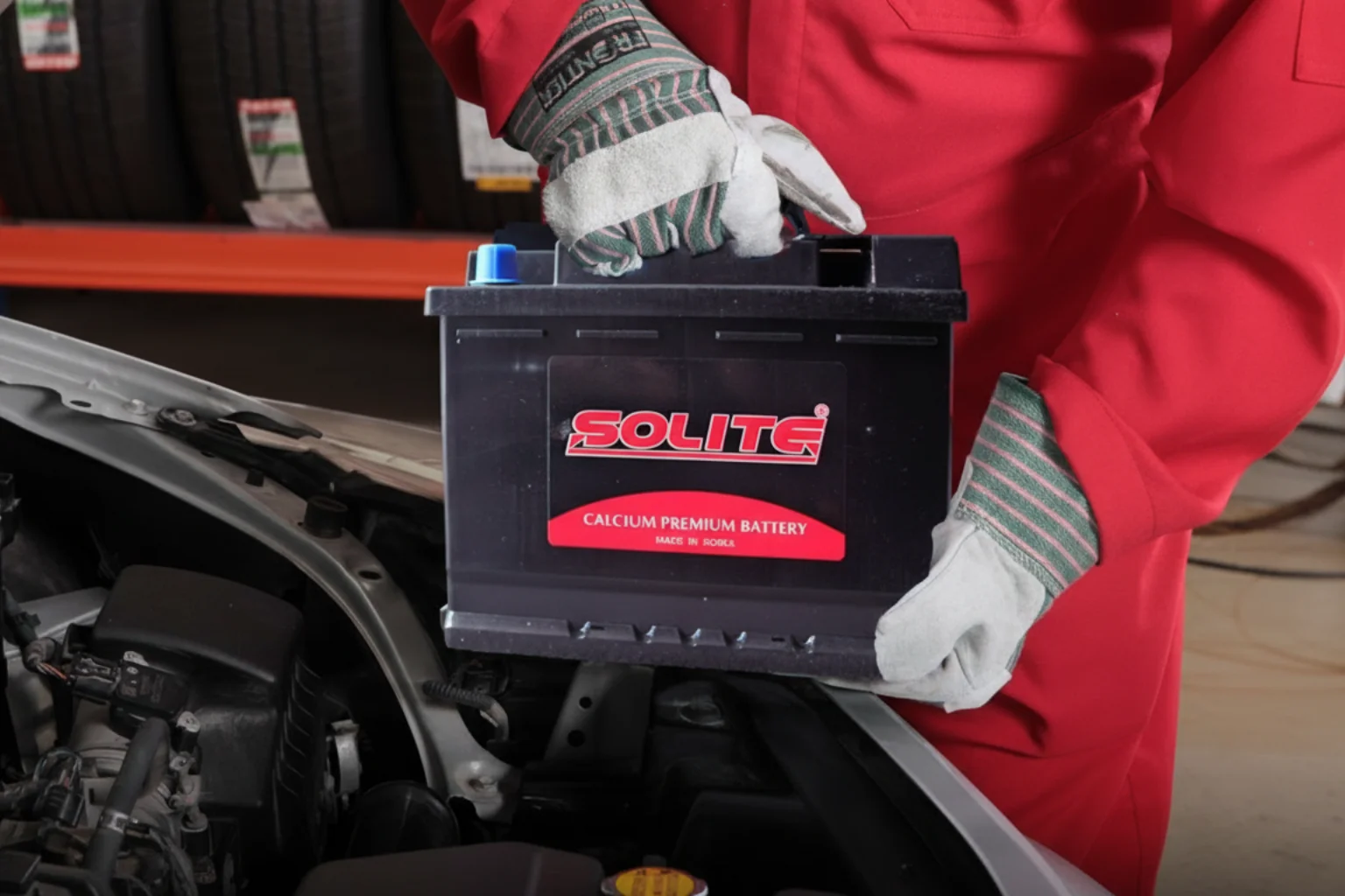 Technician in a red jacket lowering a Solite battery into a car's engine bay