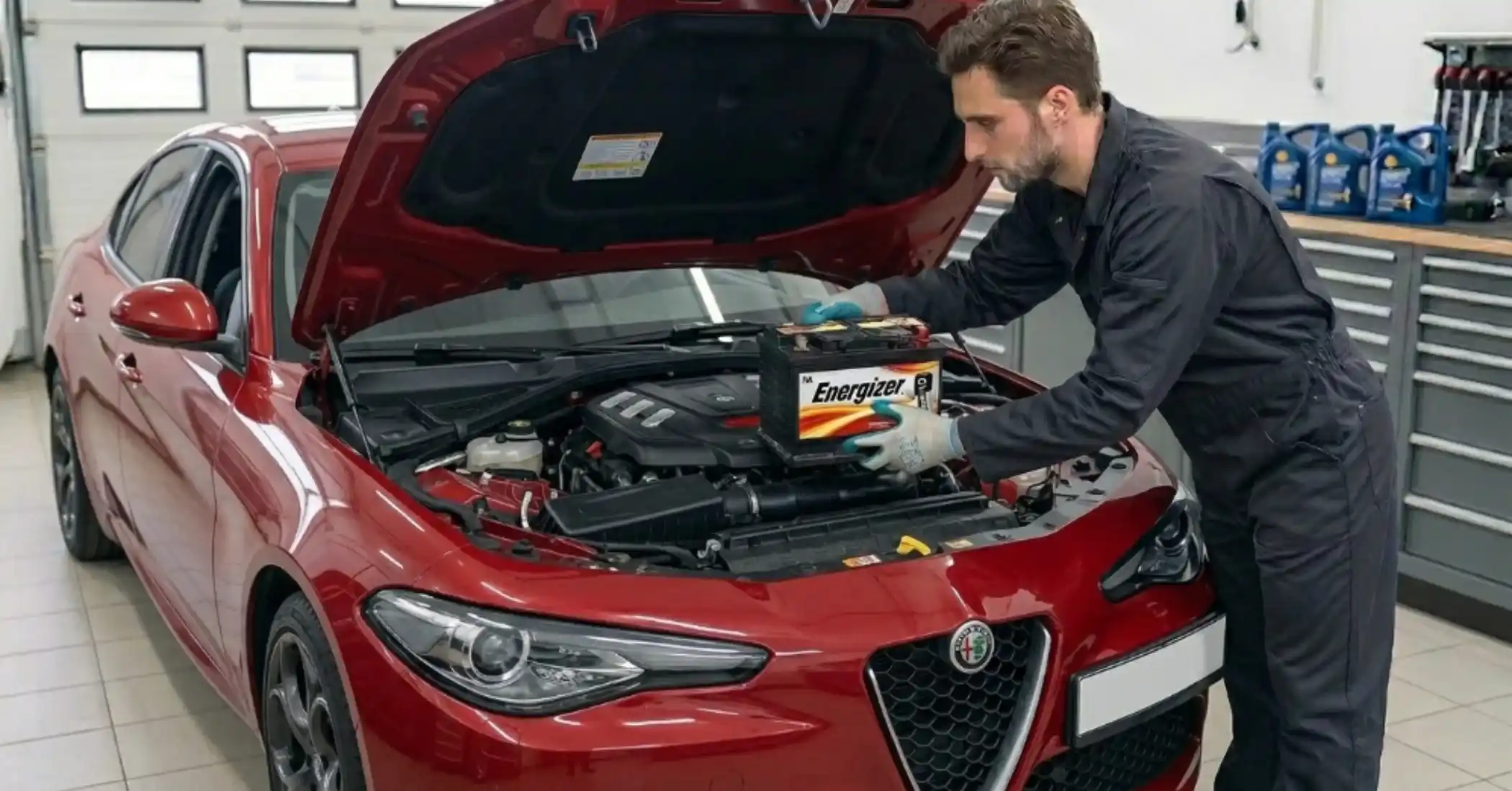 Technician lowering an Energizer battery into a red Alfa Romeo Giulia