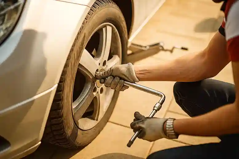 Gloved hands turning a wheel brace on the nuts of a car's wheel
